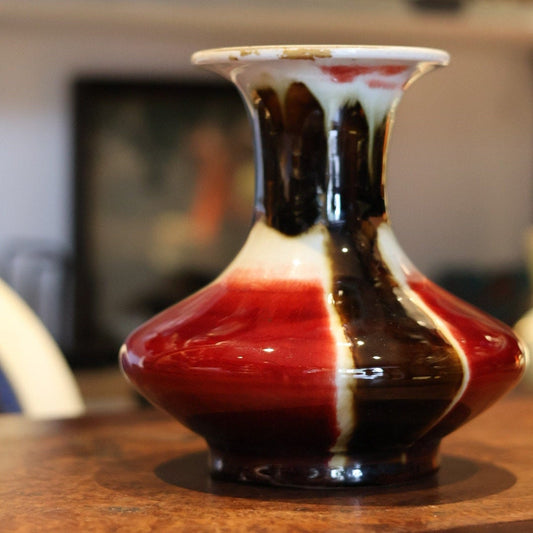 This vintage Chinese flambé glaze vase from the 1960s features an exquisite blend of red, black, and white colors. The vibrant glaze flows seamlessly, highlighting the intricate craftsmanship of Jingdezhen pottery.